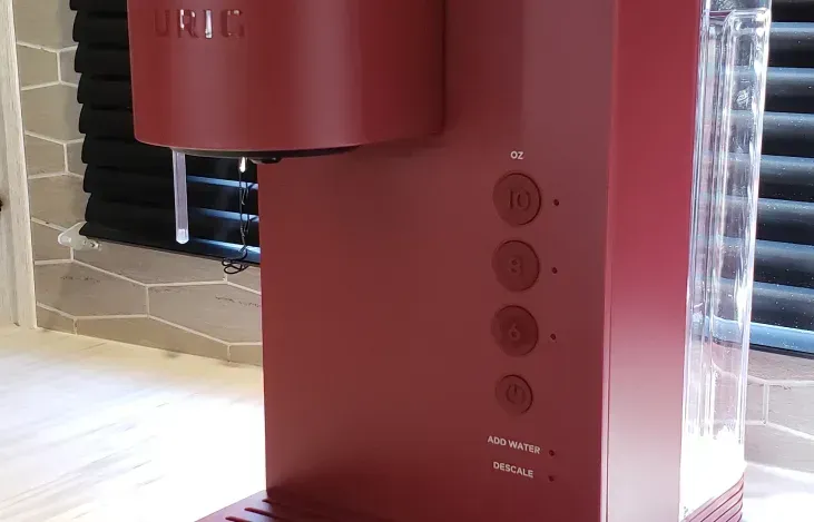 A red coffee maker is sitting on a counter next to a window.