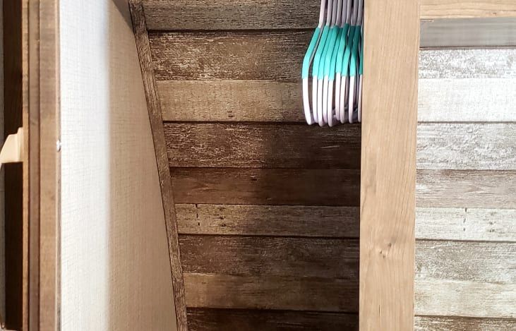 a wooden closet with a bunch of clothes hanging on the wall .