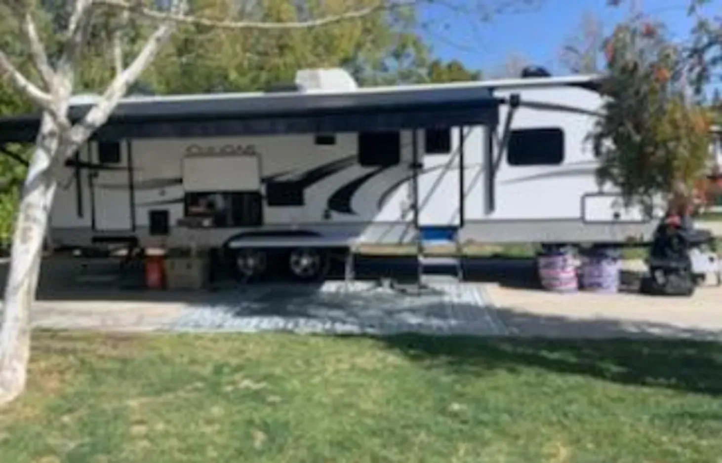 a white rv is parked in a grassy area next to a tree .