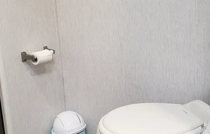 A bathroom with a toilet , trash can , and paper towel holder.
