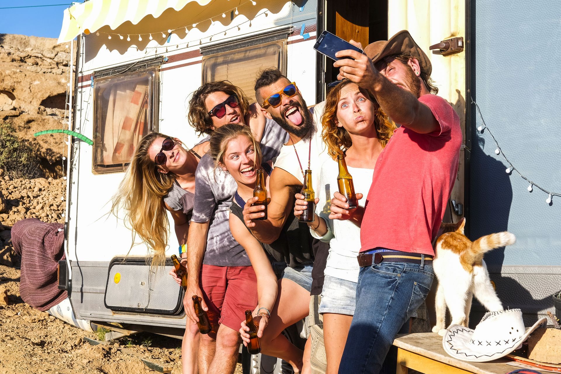 group young people friends taking selfie picture using mobile phone outside caravan trailer making funny faces holding beer bottle group young people friends taking selfie picture using mobile phone outside caravan trailer.