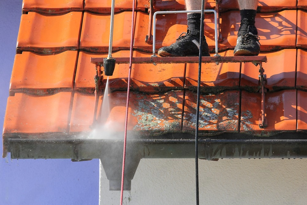 a person on a ladder cleaning a roof with a high pressure washer