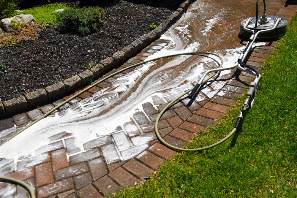 A circular pressure washer cleans a decorative brick sidewalk, creating a mesmerizing pattern with soapy water.