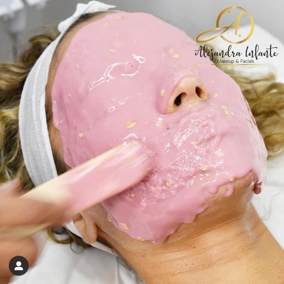 A woman is getting a pink mask on her face.