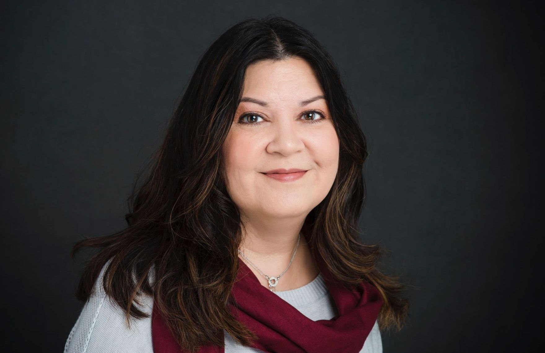 A woman wearing a scarf and a necklace is smiling for the camera.
