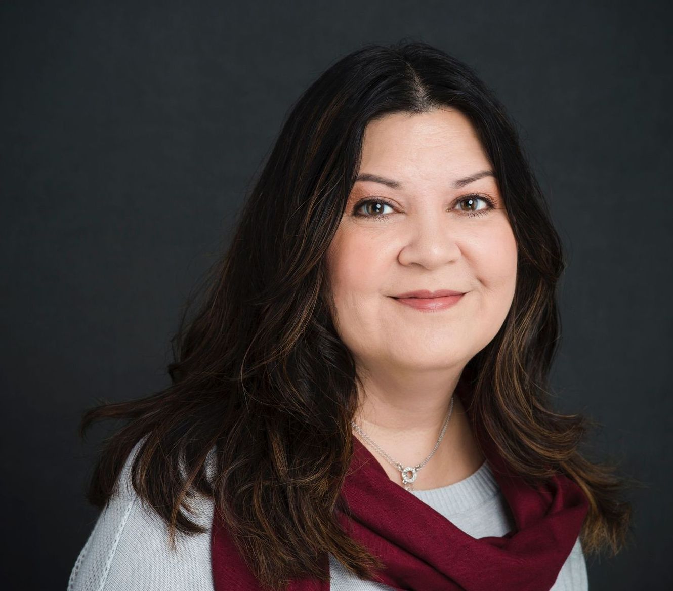 A woman wearing a scarf and a necklace is smiling for the camera.