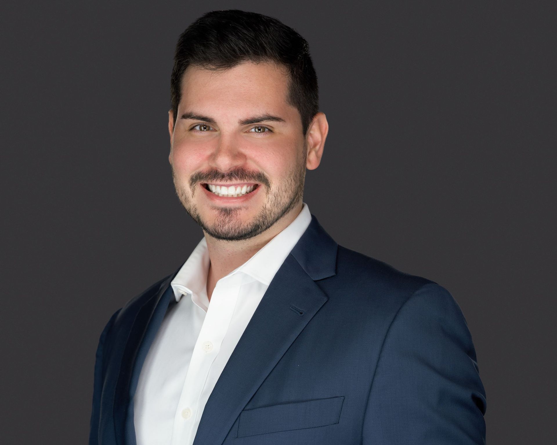 A man in a suit and white shirt is smiling for the camera.