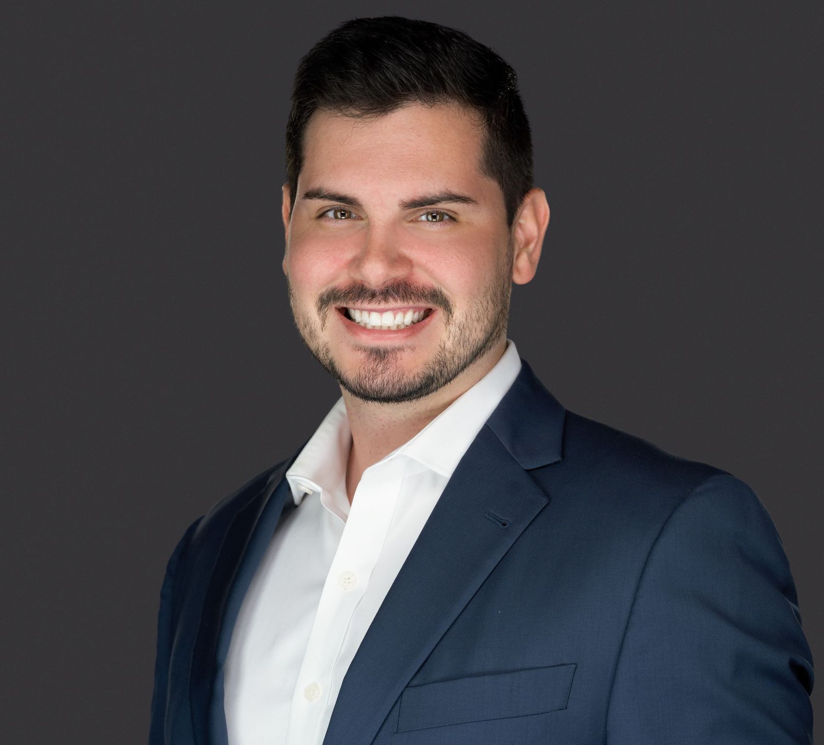 A man in a suit and white shirt is smiling for the camera.