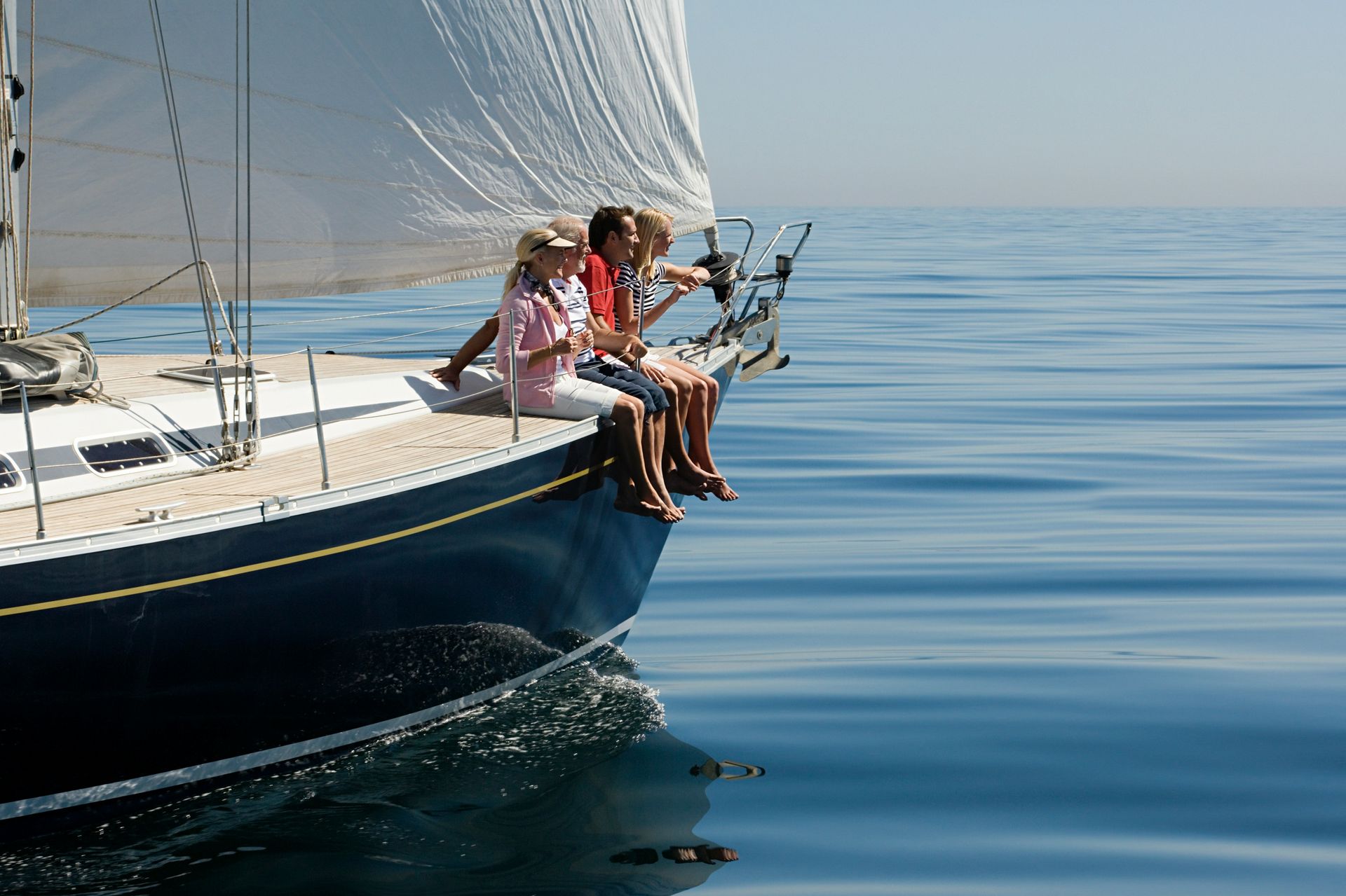 A group of people are sitting on the bow of a sailboat in the ocean.