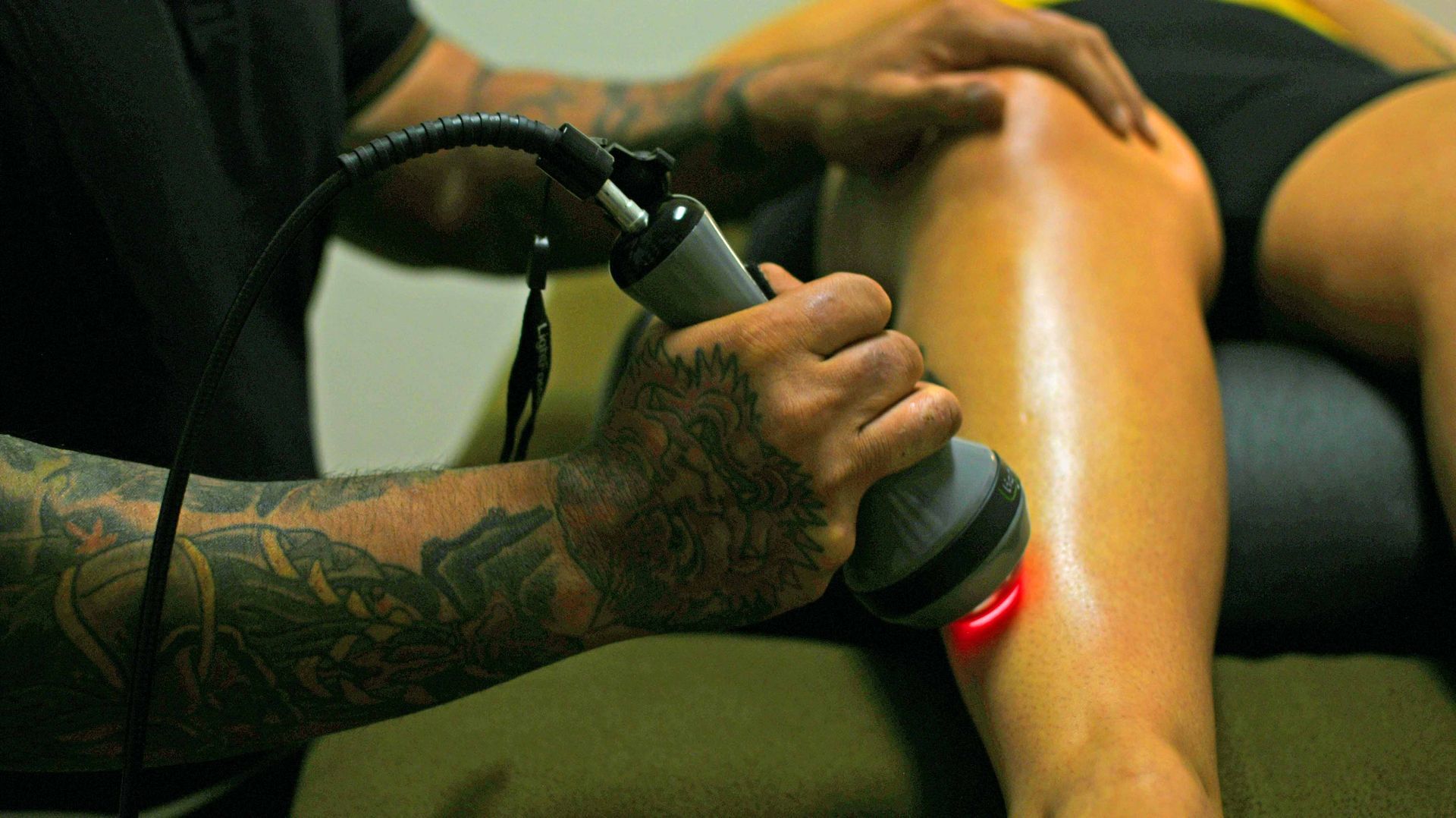 A person holding a laser and administering class IV laser to a person's lower leg