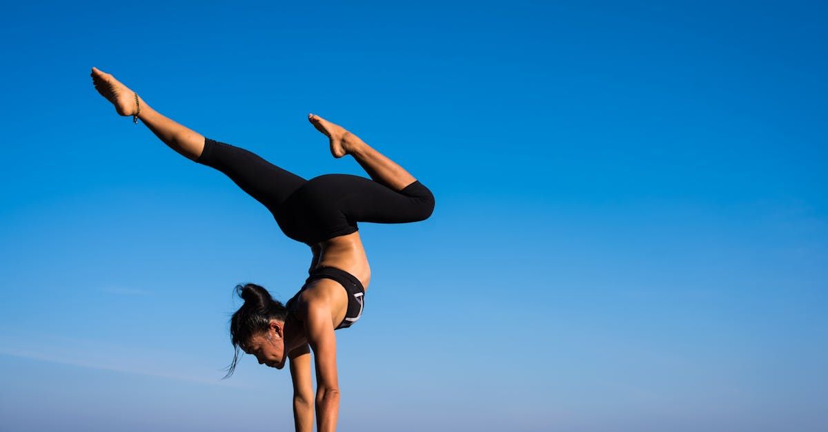 A woman is doing a handstand in front of a blue sky.