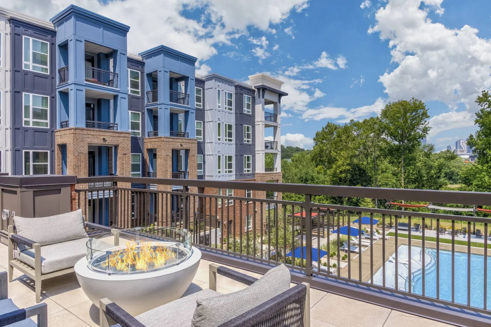 Balcony view of a modern blue-gray apartment complex with a pool and lounge area.