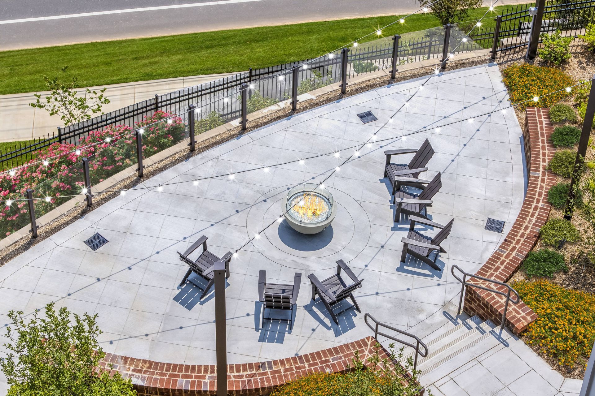 Outdoor patio with fire pit, seating, string lights, and brick edging.