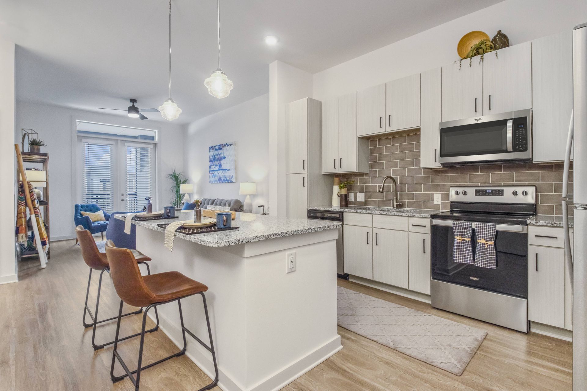 Modern kitchen with white cabinets, stainless steel appliances, and a granite island with brown leather stools.