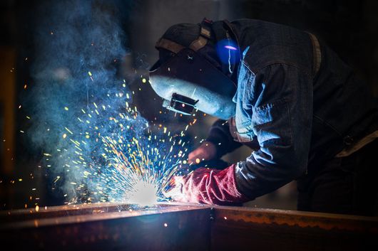 A man wearing a welding mask is welding a piece of metal.