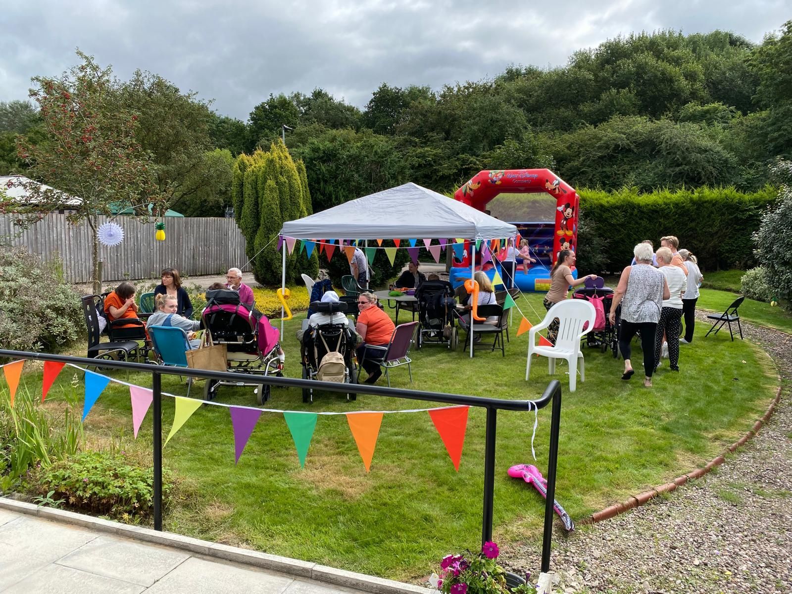 Outdoor event with a tent, bouncy castle, and people in wheelchairs; colorful flags.