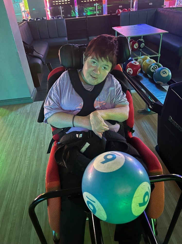 Person in a wheelchair holding a blue bowling ball with a nine. Inside a bowling alley.