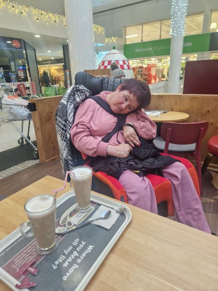 Woman resting in a mall cafe chair with two hot drinks on a tray.