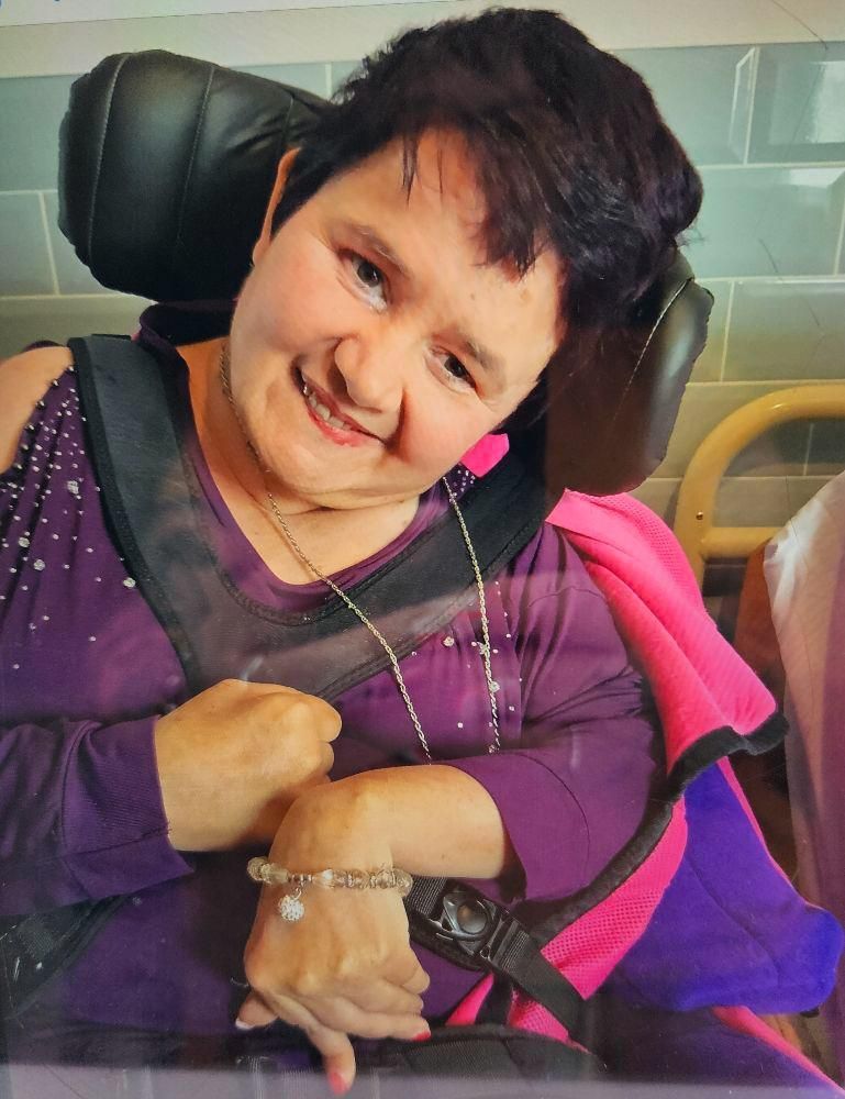 Woman in wheelchair smiling, wearing purple and pink clothing.