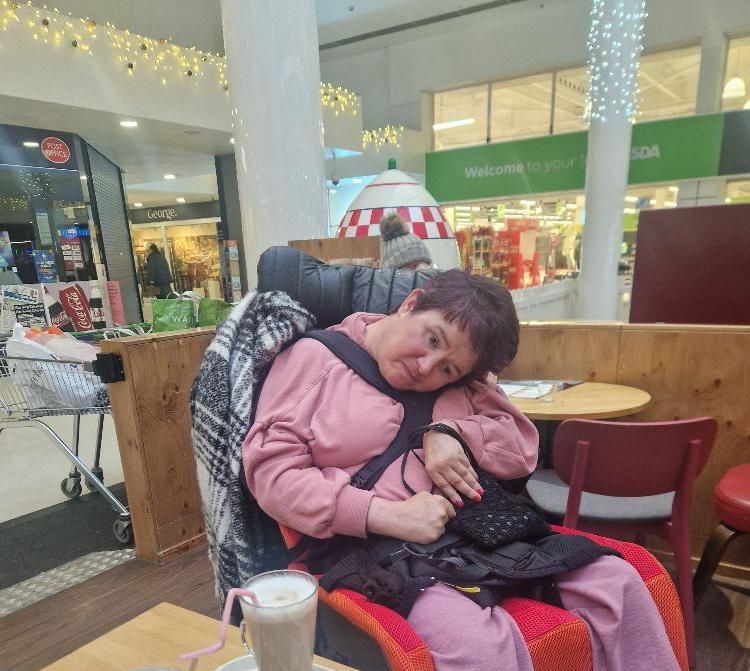 Woman in a pink top and blanket, sitting in a chair indoors with a drink.
