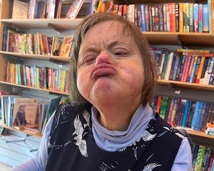 Woman with Down syndrome puckers lips, standing in a bookstore.