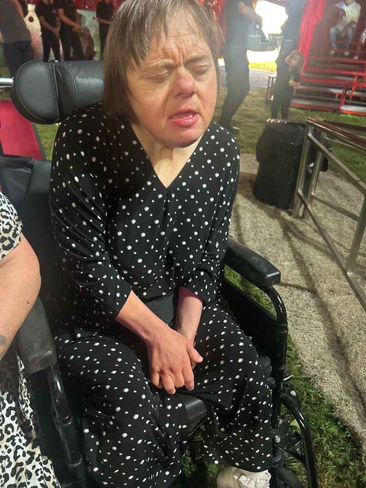 Woman with Down syndrome in a wheelchair, wearing black polka dot outfit, at an outdoor event.