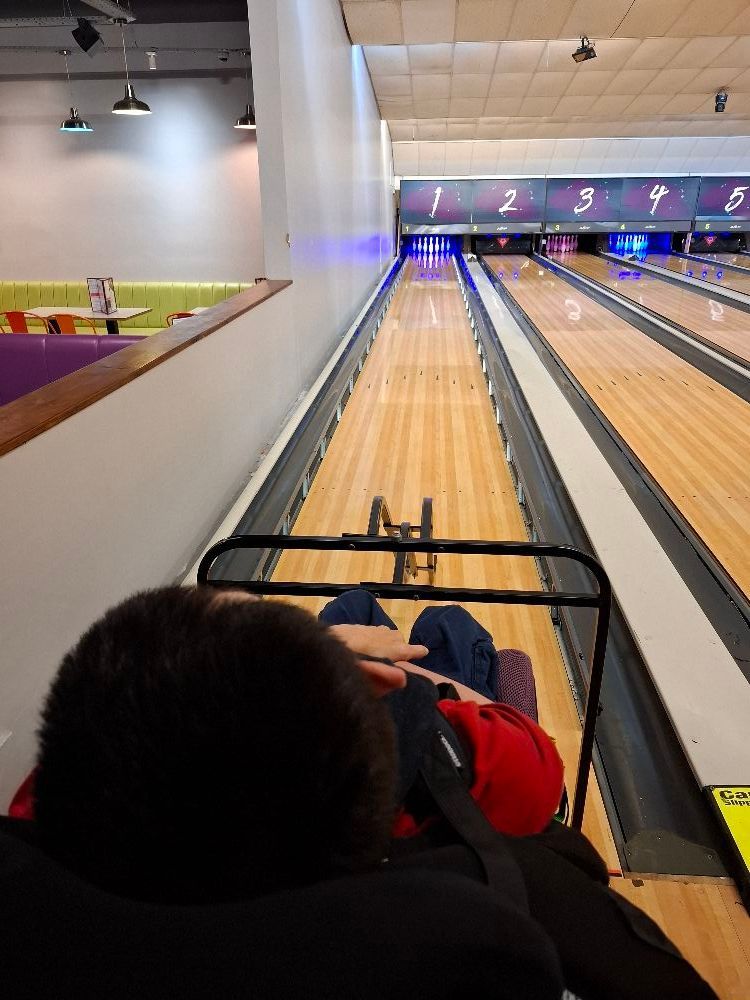 Person in a wheelchair at bowling alley. They are facing the lanes, ready to bowl.