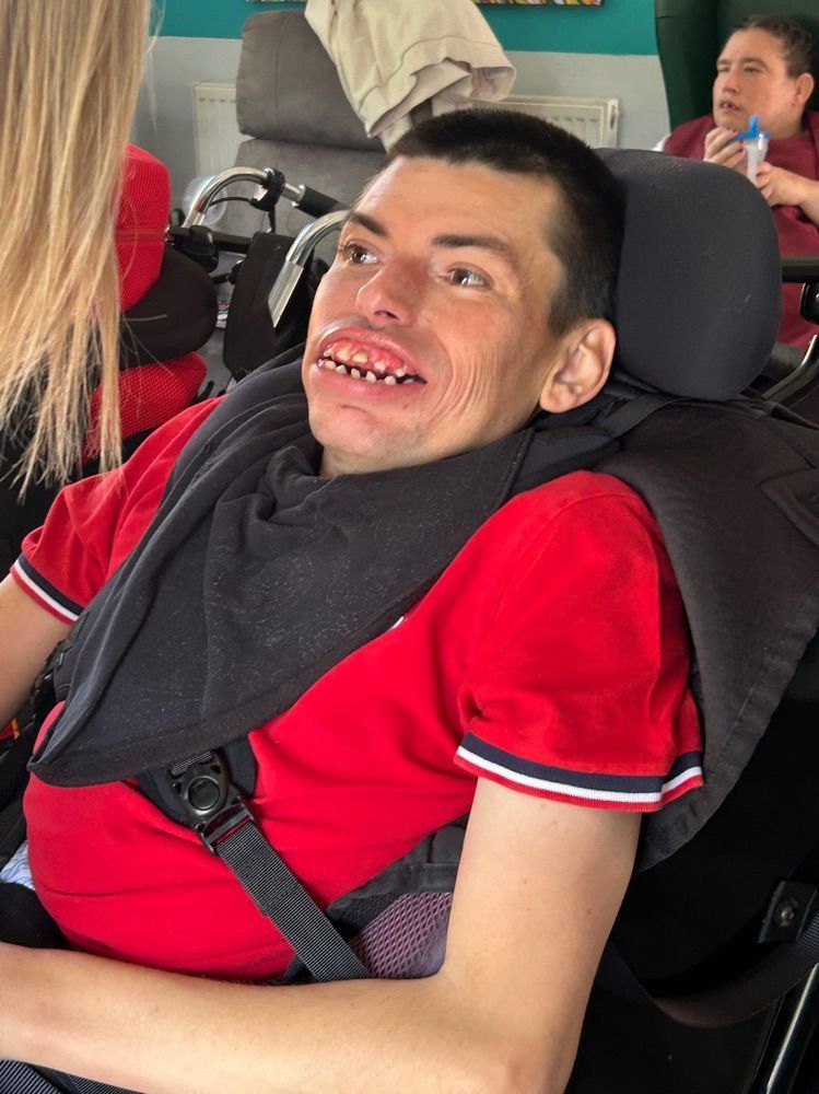Man in a wheelchair smiles, wearing a red shirt. Indoors.
