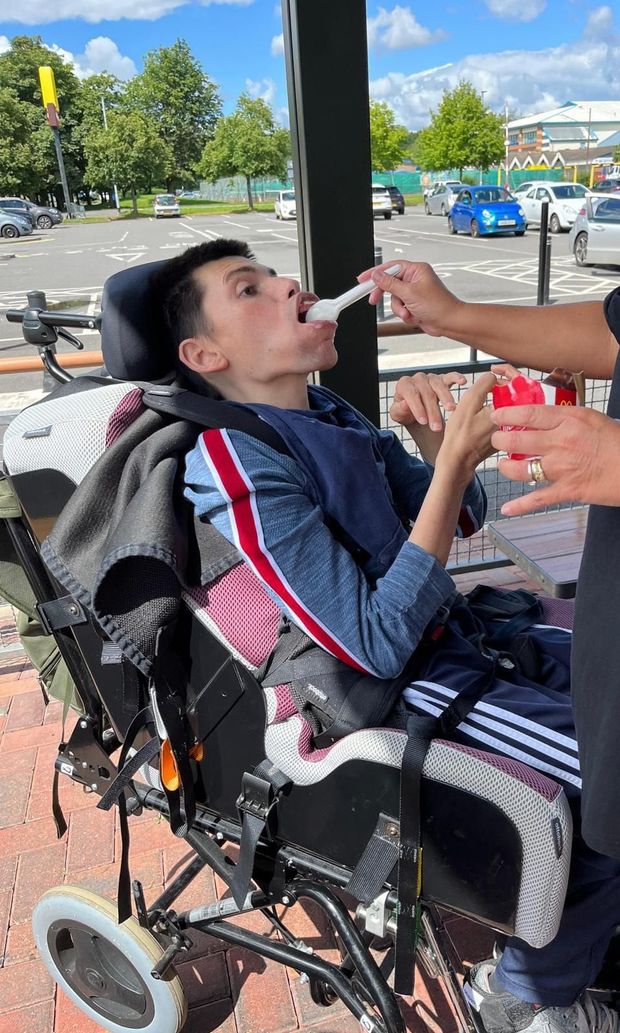 Person in a wheelchair being fed ice cream outside a restaurant. Sunny day.