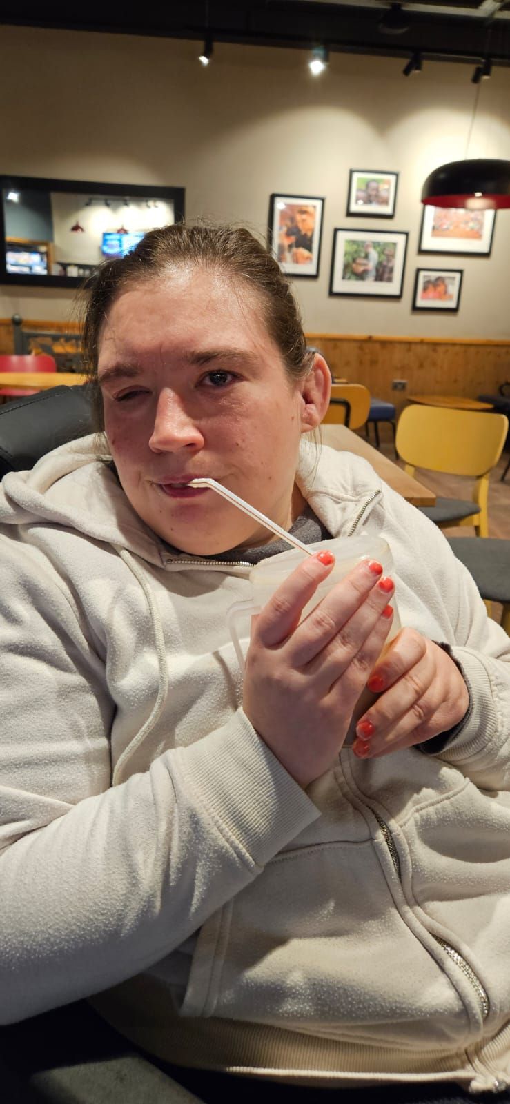 A person in a light hoodie is drinking with a straw. They are in a cafe.