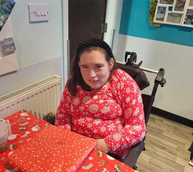 Woman in wheelchair at a table, wearing red snowflake shirt, black headband. Indoors with presents.
