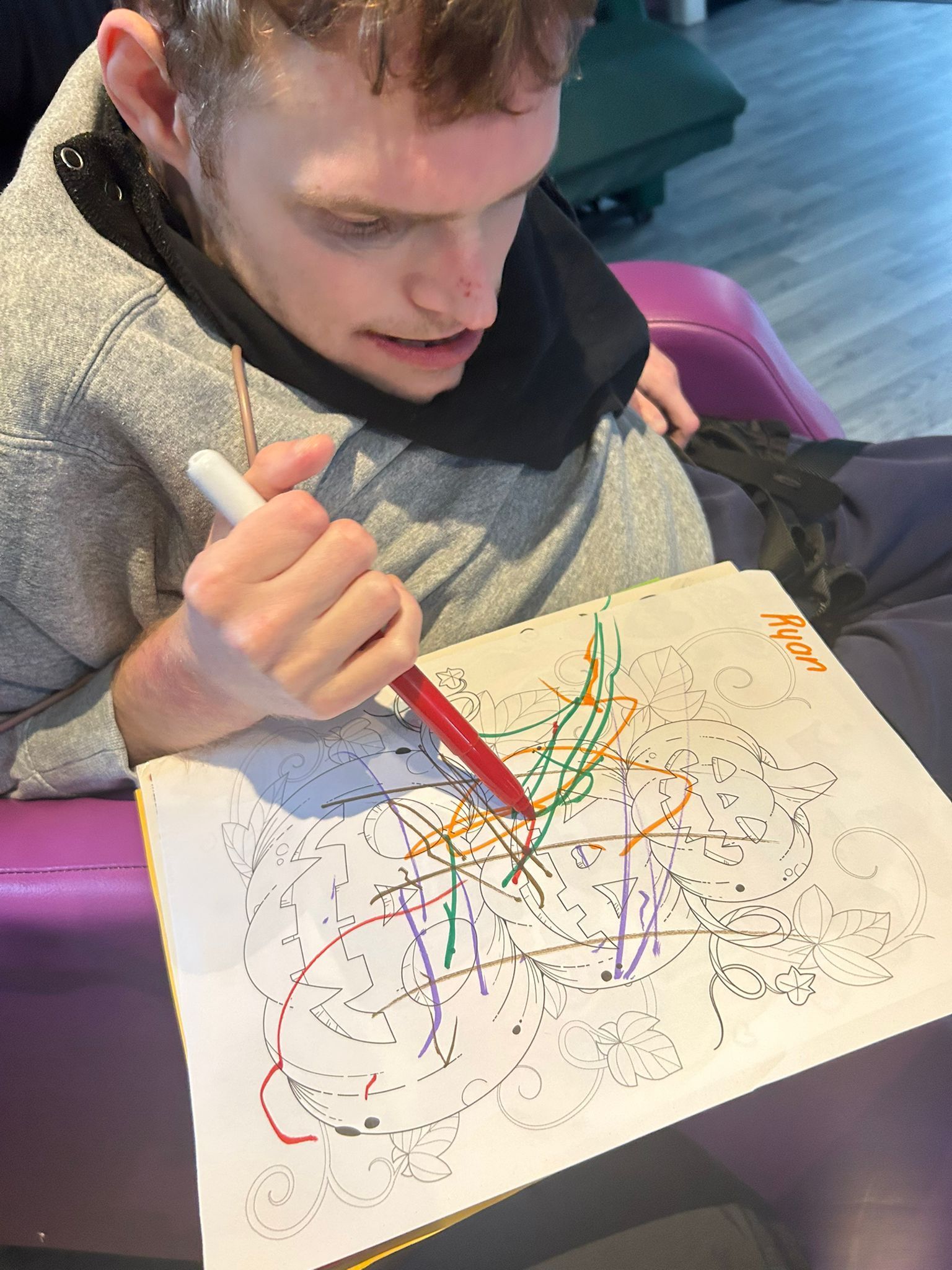 Young person drawing with colorful markers, focused expression. Indoors, seated, casual wear.