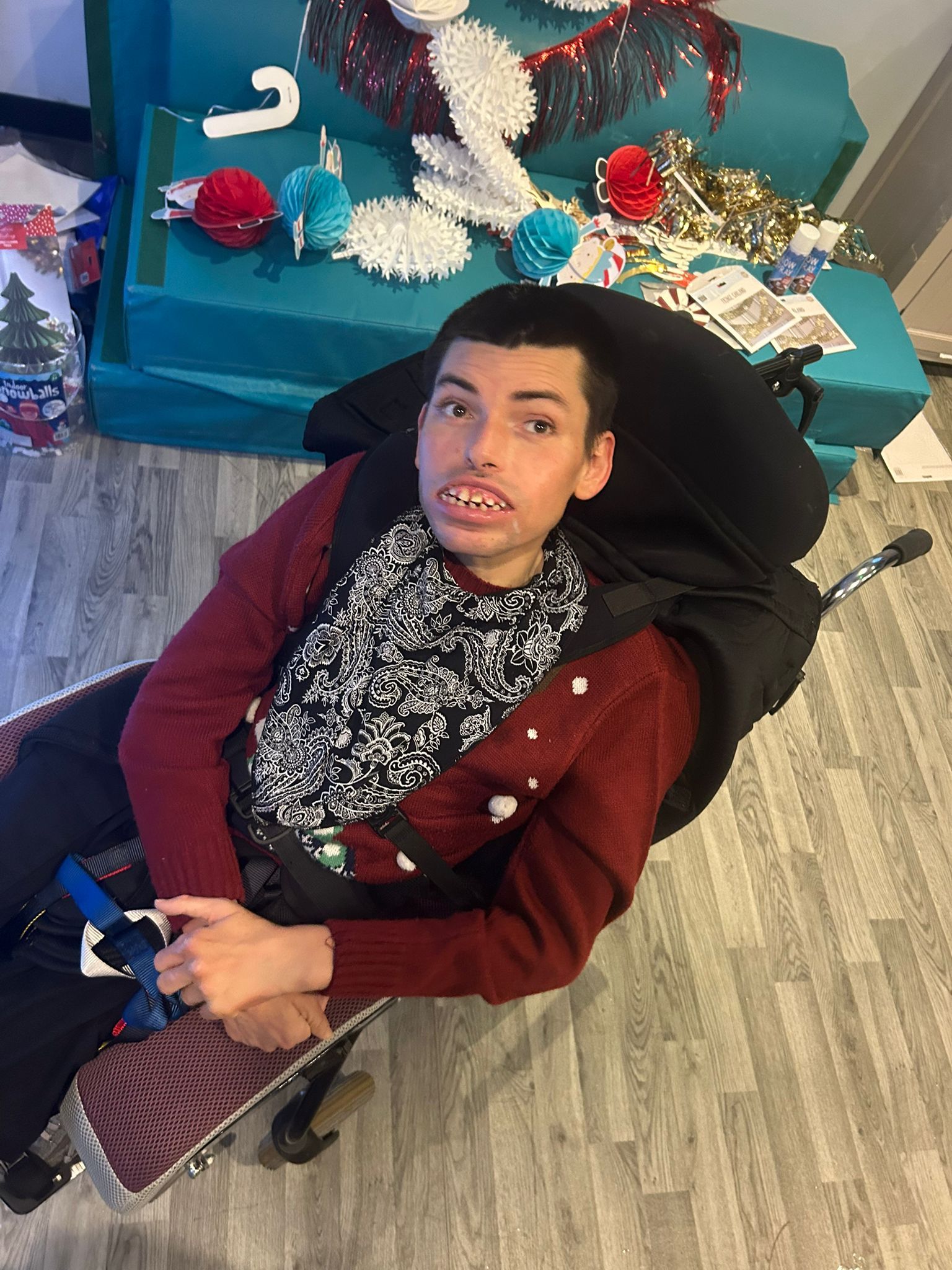 Person in a wheelchair, wearing a red sweater, in a room with Christmas decorations.