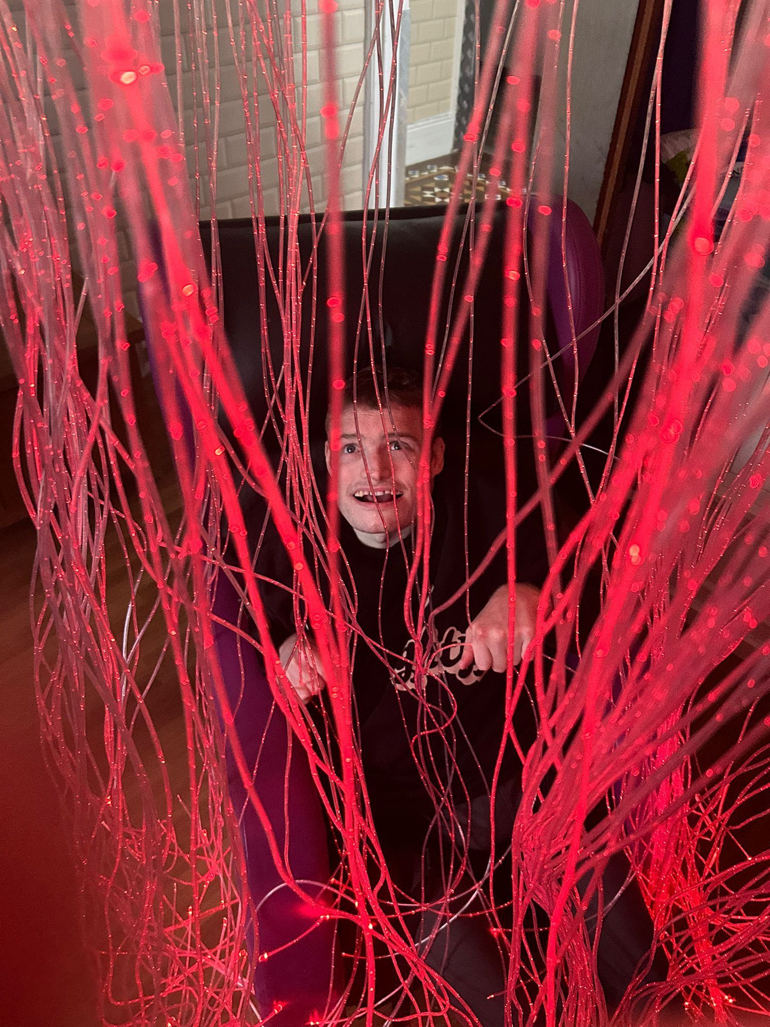 Man seated in chair, surrounded by red, glowing strands; surprised expression.