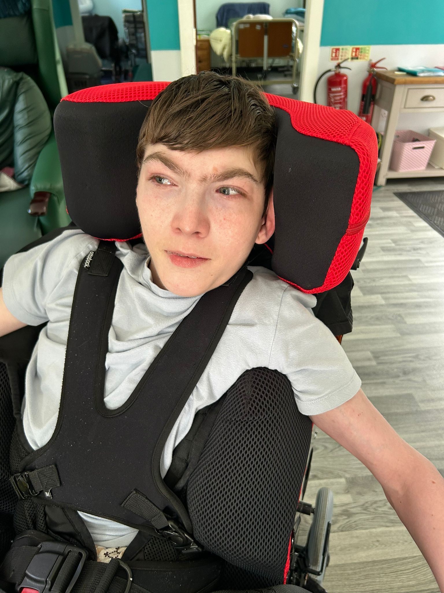 Young man in wheelchair with headrest, wearing a gray shirt, looking slightly to the side.