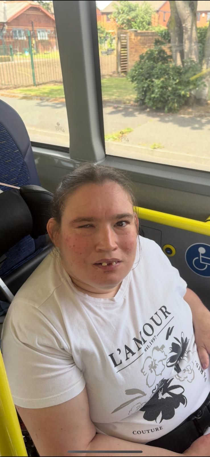 Person sitting on a bus, wearing a white t-shirt with the word “L'AMOUR”, looking towards the camera.