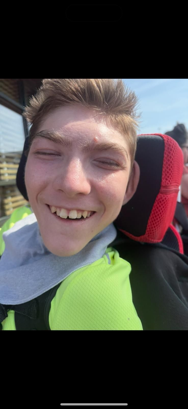 A smiling young man outdoors, wearing a light green shirt, sitting in a wheelchair.