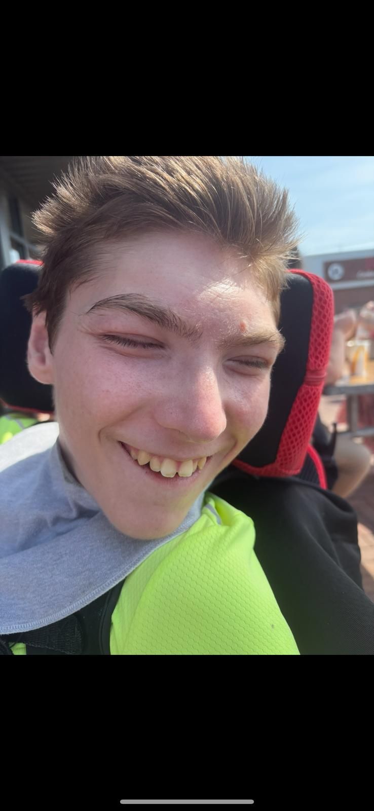 A smiling person in a wheelchair wearing a grey shirt and neon green shirt.