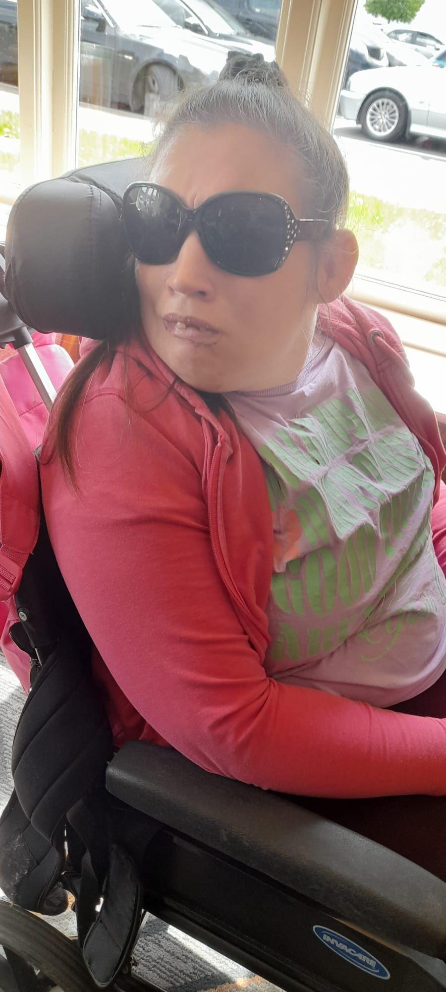 Person in a wheelchair wearing sunglasses and a red jacket outside.
