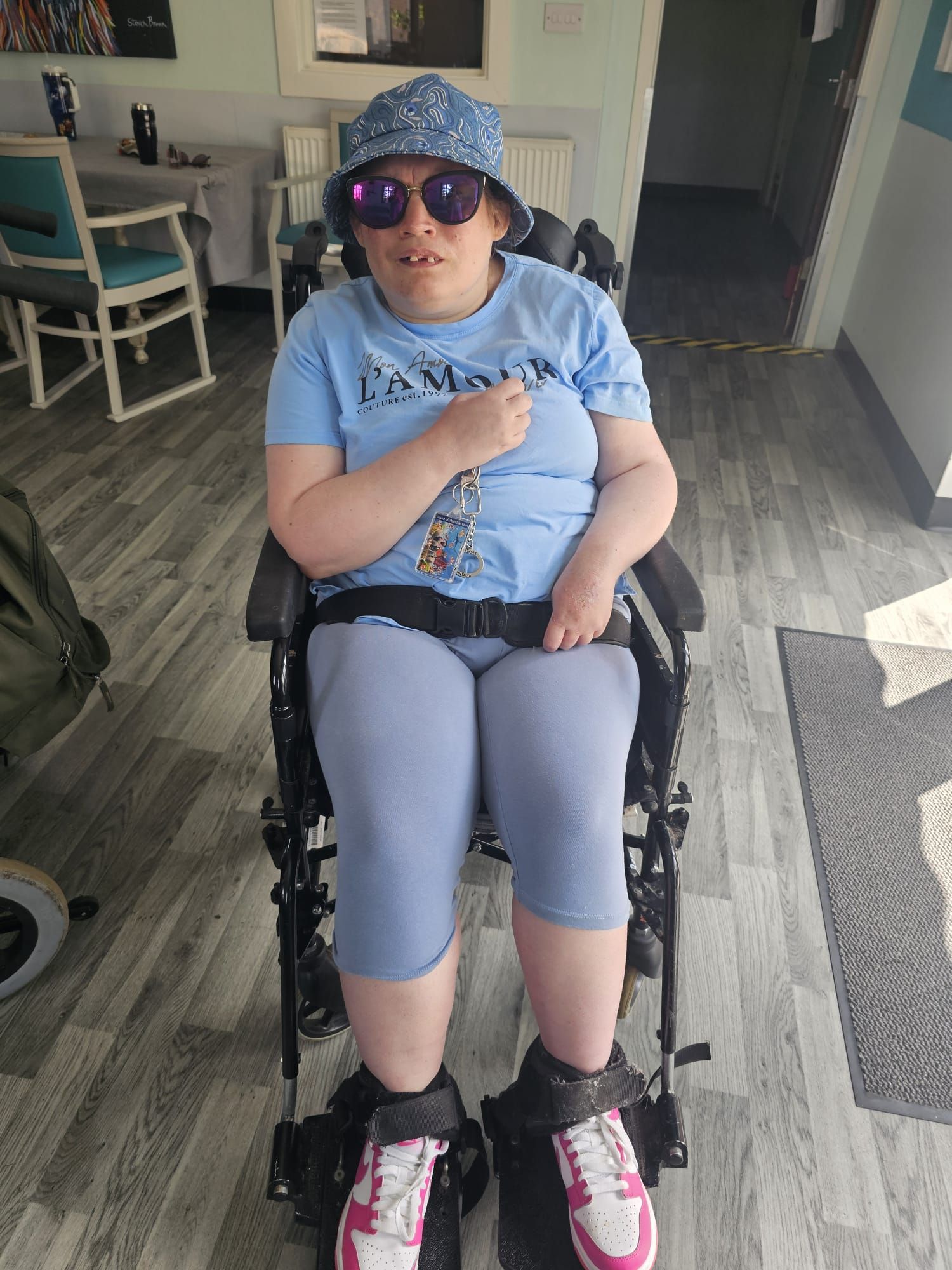 Woman in wheelchair wearing sunglasses and a hat, sitting indoors.