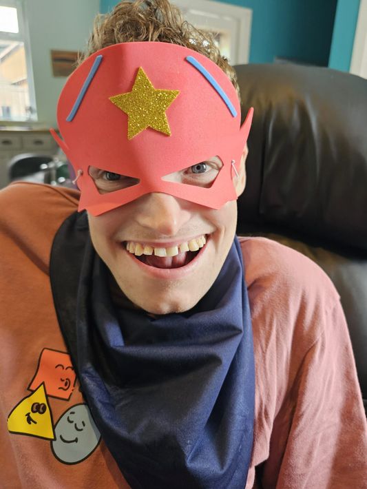 Man wearing a superhero mask and scarf, smiling widely; indoors.