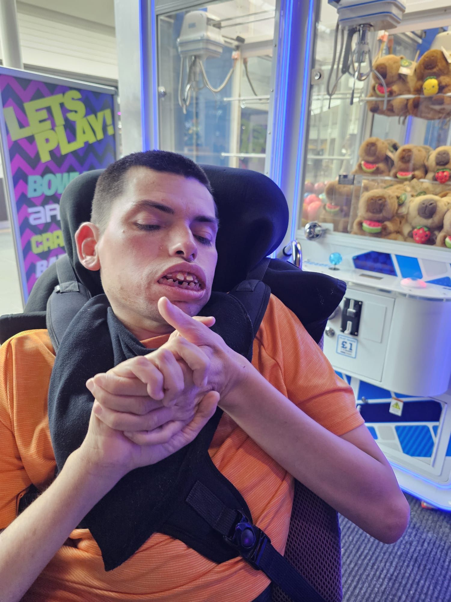 Man in a wheelchair pointing fingers, in front of a claw machine with stuffed toys.