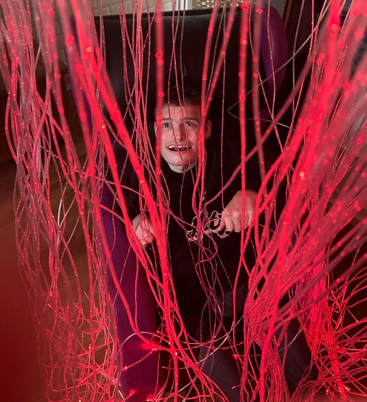 Man playing with a sensory curtain in red. Dark setting.