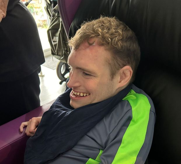 Man with curly hair smiling, wearing a gray and green athletic shirt, sitting indoors.