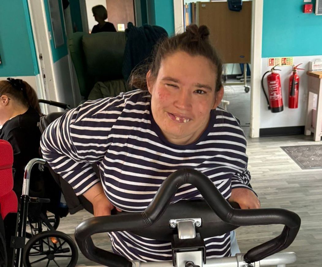 Person with disability smiling, using exercise equipment, indoors. Wearing striped shirt.