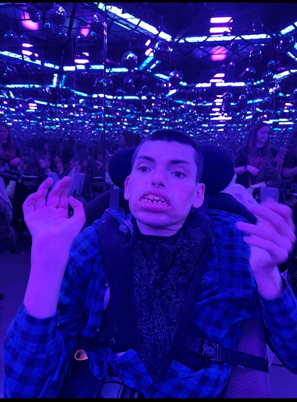 Person in wheelchair with purple lighting, making hand gestures, in a dark hall with lights.