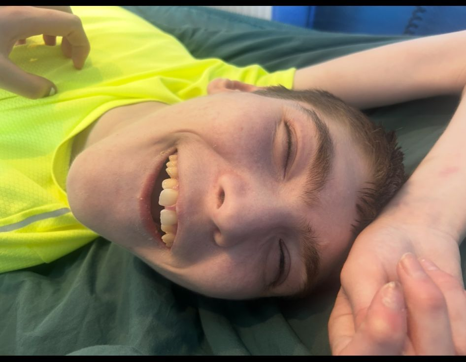 Smiling person in a neon yellow shirt lying down, eyes closed. Hand touches the person's chest.