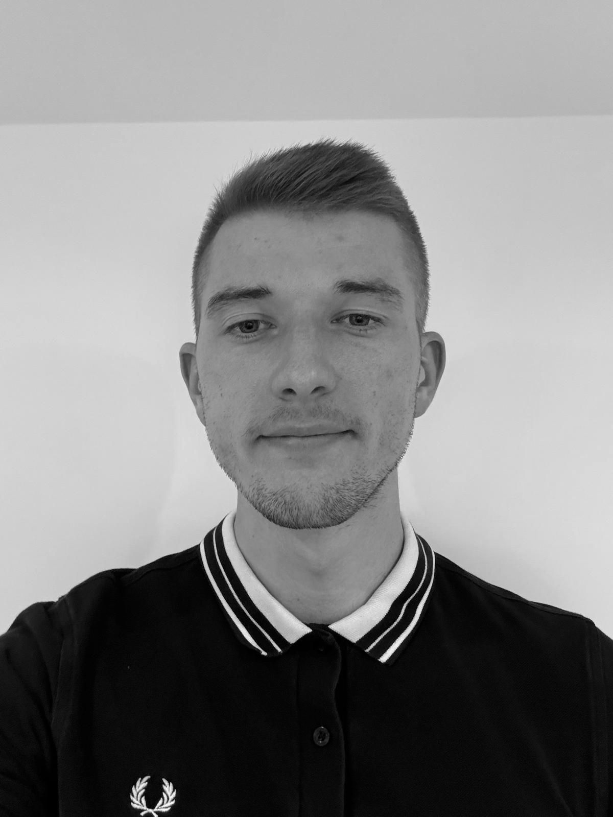 Man in black polo shirt with white collar and Fred Perry logo, neutral expression.