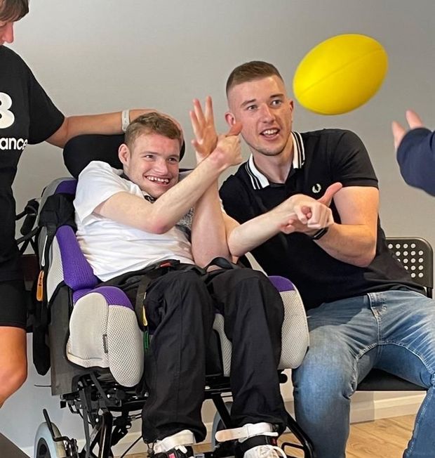 Man in wheelchair high-fives another as a yellow ball flies by. Others nearby.