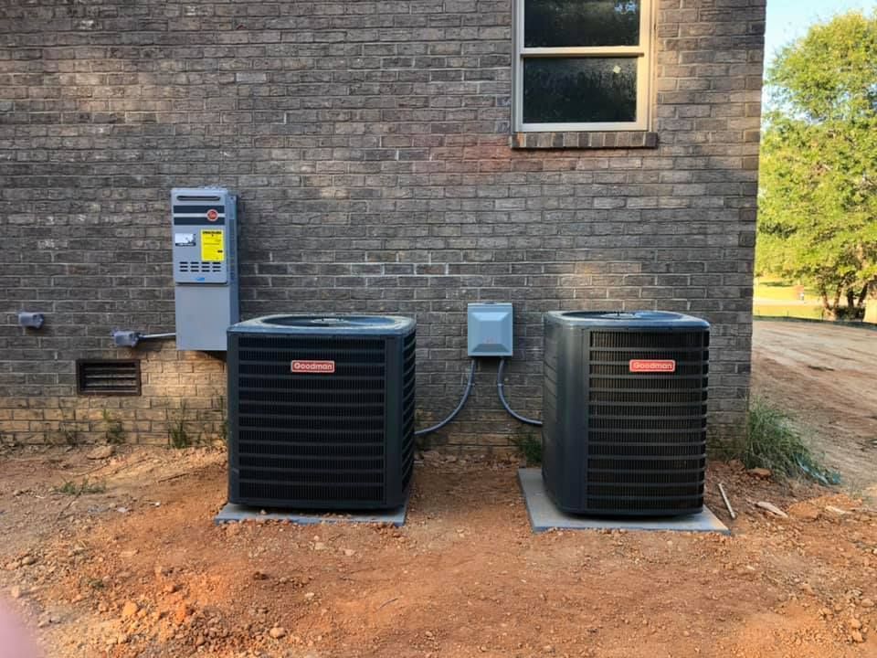 Two air conditioners are sitting on the side of a brick building.